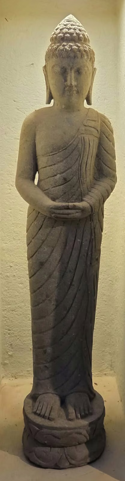 A tall standing stone Buddha lit within a wall niche