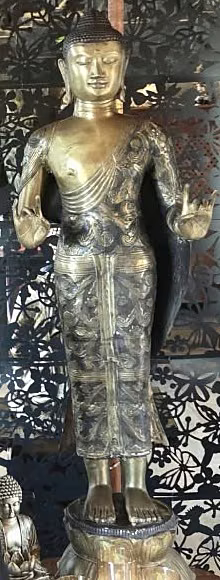 A tall gilded standing Buddha against the carved screen in the restaurant