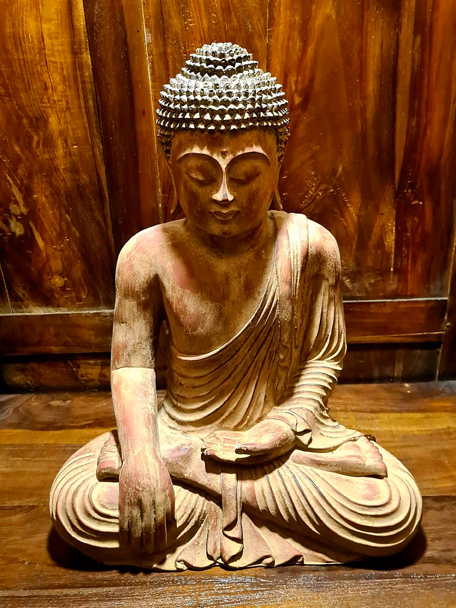 A carved and painted wooden Buddha against a timber wall