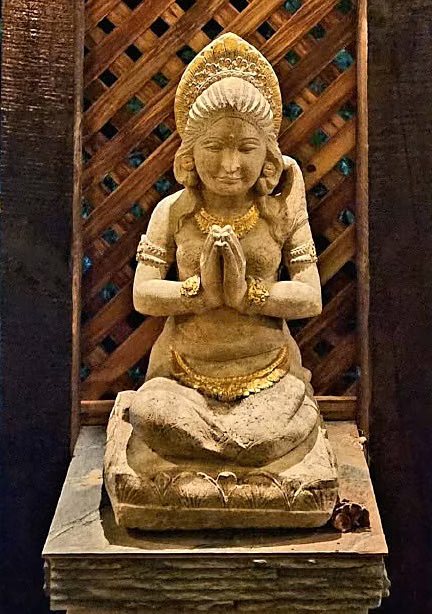 A kneeling stone figure with gold leaf, hands together, before a carved screen