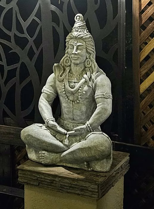 A seated stone Shiva against a carved screen