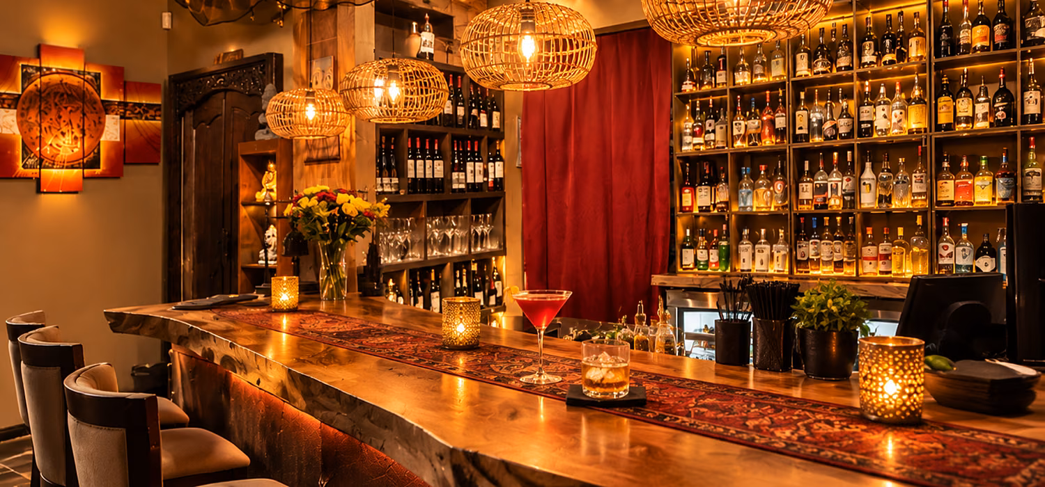 The bar counter at night, backlit shelves and rattan pendants above