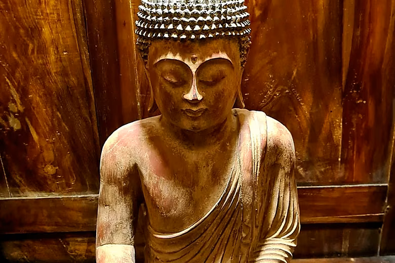 A carved and painted wooden Buddha against a timber wall