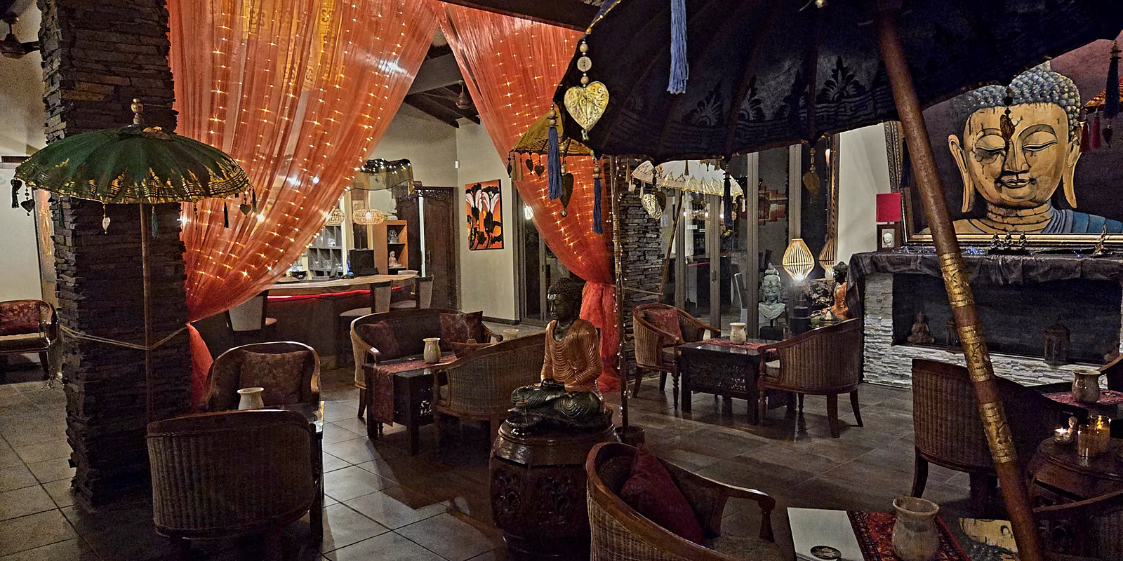 The lounge beneath Balinese parasols, with the Buddha mural and fireplace beyond