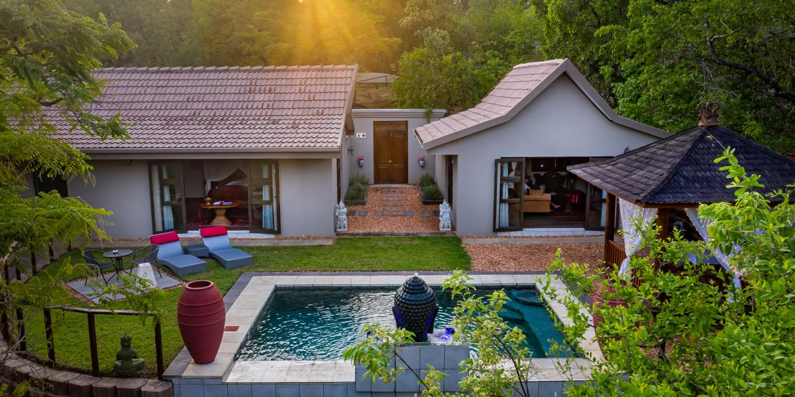 A villa and its private rim-flow pool at sunset, with the sun low through the trees
