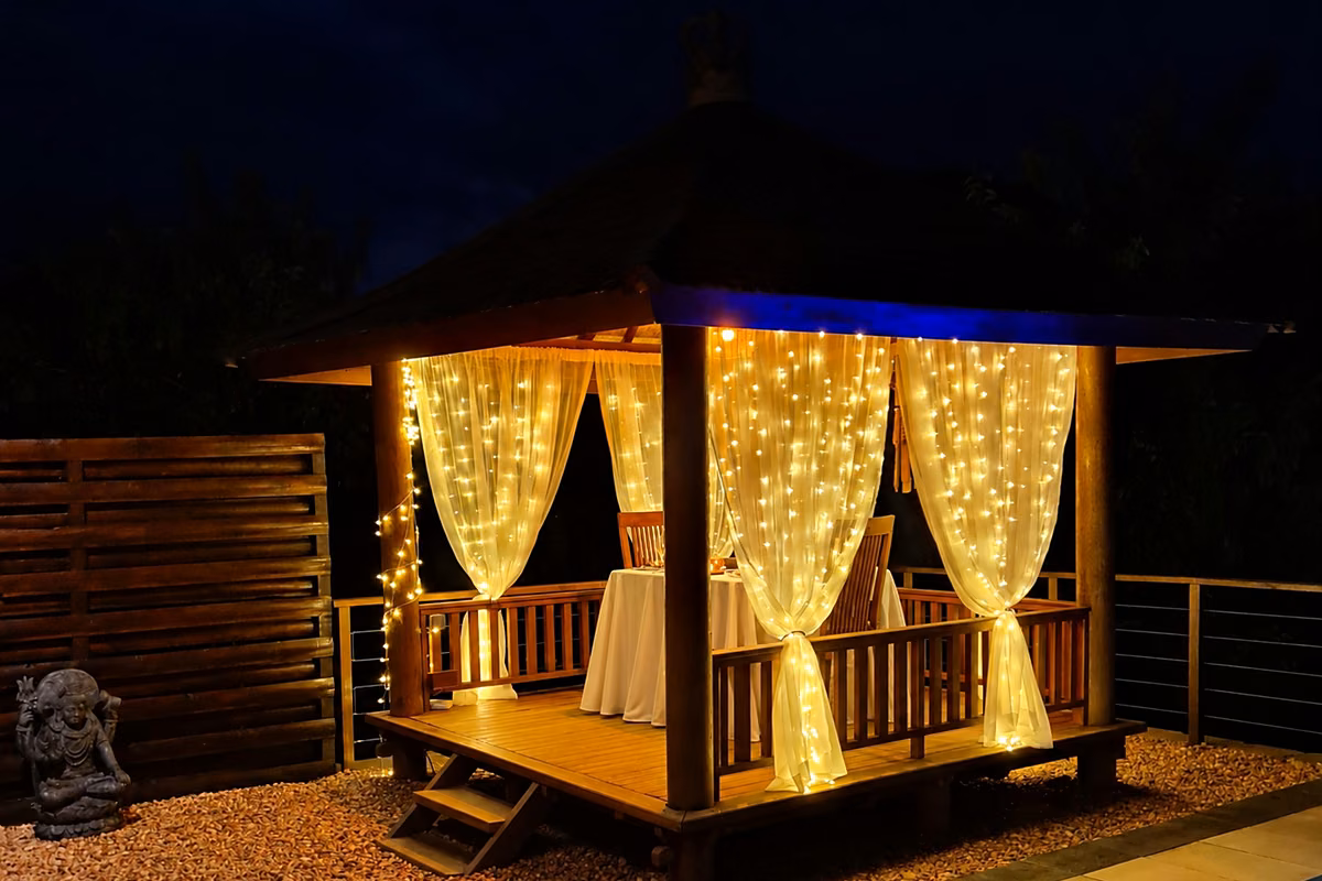 The private dining gazebo at night, curtained in fairy lights, with the table laid inside