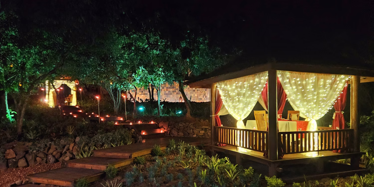 The private dining gazebo at night, draped in fairy lights, with lantern-lit steps leading up through the garden